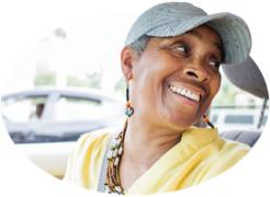 A woman in a ballcap turns and grins at her backseat passenger.